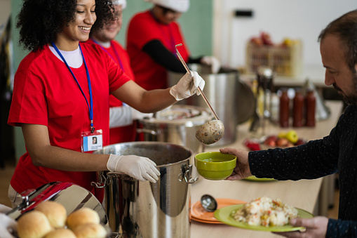Cheerful aid workers are serving hot and healthy food in a soup kitchen to poverty stricken and hungry people