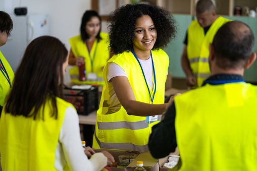 A group of young volunteers working together packing food donations into grocery boxes ready for distribution, wearing fluorescent jackets while they work for a community outreach program