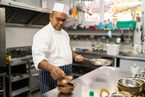 After filling a balti bowl with tasty curry, the professional chef is placing the lid to keep it warm in a commercial Indian kitchen