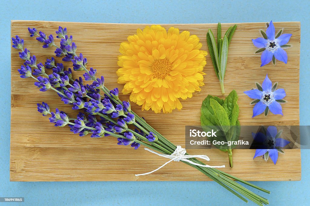 Summer herbs and edible flowers on wooden plate. Summer herbs and edible flowers on wooden plate on blue background. Lavender (Lavandula), marigold (Calendula officinalis), Rosemary, Mint and borage (borago). Also beauty care. Aromatherapy Stock Photo