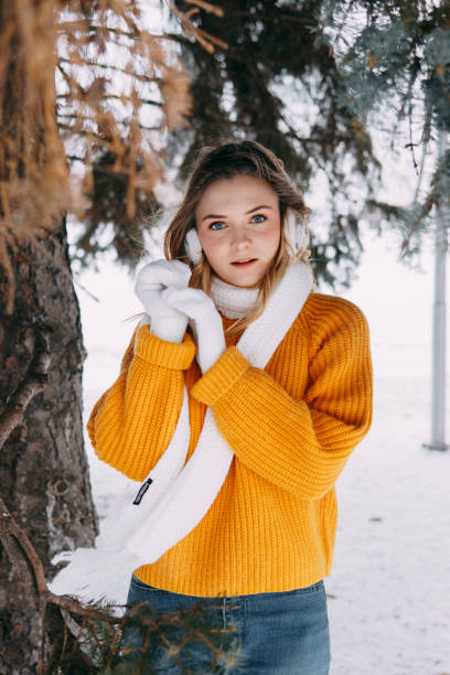 Teen blonde in a yellow sweater outside in winter. A teenage girl on a walk in winter clothes in a snowy forest stock photo