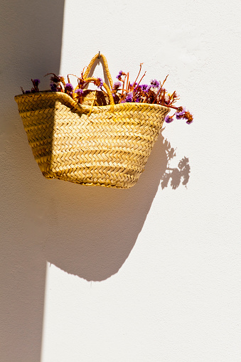 Basket with flower bouquet hanging from white wall, sunlight, shadow. old town Valença do Minho, Portugal.
