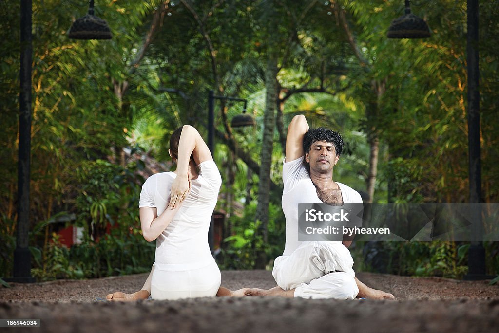 Couple yoga gomukhasana cow pose Couple Yoga of man and woman doing gomukhasana cow face pose front and back sides in white cloth in the garden Yoga Stock Photo