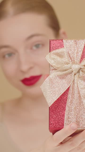 Zoom IN Effect. Portrait of a delightful woman with red lips, gives a red gift box.