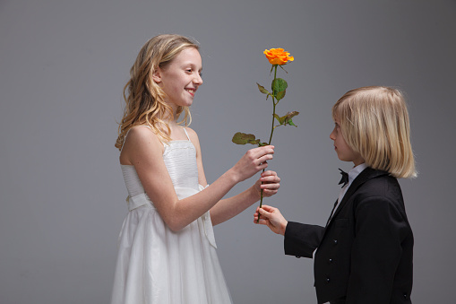 Boy giving his girl orange rose for birthday or valentine's day. Isolated on dark background.