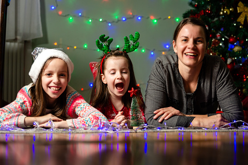 Portrait of a happy mother whit her two daughters lying on the floor and looking at camera during Christmas night