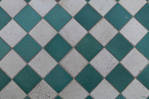 High-angle view of a mosaic of a vintage, diamond pattern layout of green and white floor tiles.