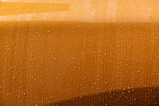 Abstract detail of water and raindrops neatly collected on the gold, metal frame of an automobile