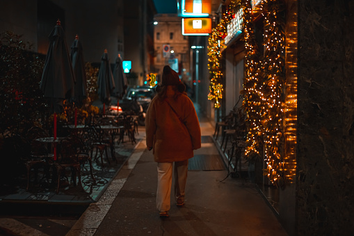 A young woman walks through the streets of evening Milan. Beautiful showcases decorated with garlands. Christmas atmosphere