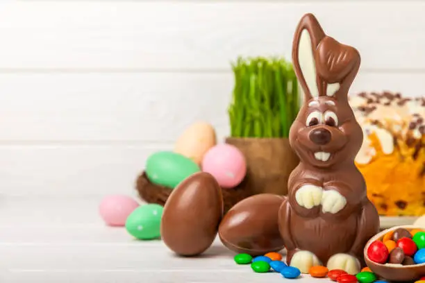 Photo of Easter chocolate bunny on a light texture table. Chocolate eggs and other sweets. Easter celebration concept. Easter sweets on the table. Place for text. copy space.