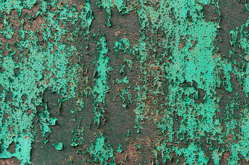 Bright green cracked and peeling paint on a detail of a section of a metal fence.