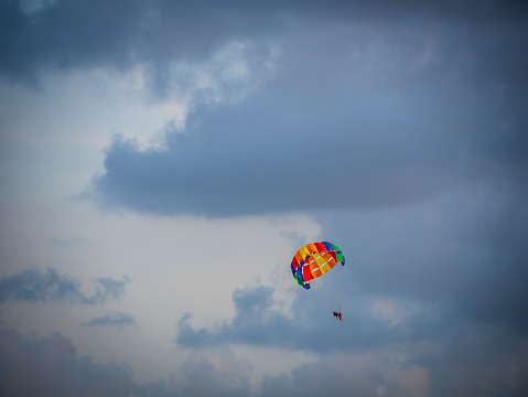 Goa, India - May 22, 2022: Unidentified tourists enjoying parasailing with colourful parachute at south Goa beach.