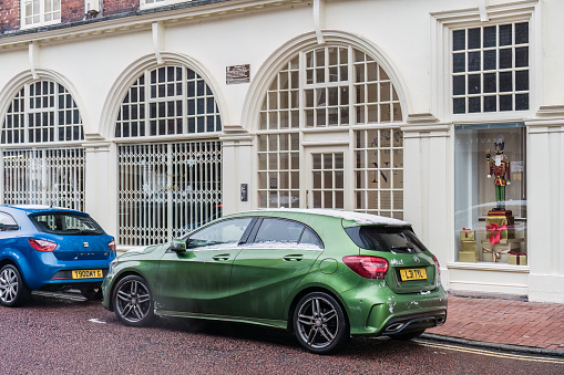 Nantwich, Cheshire, England, December 3rd 2023. A green Mercedes-Benz A-Class parked on a street in front of a classic arched window display.