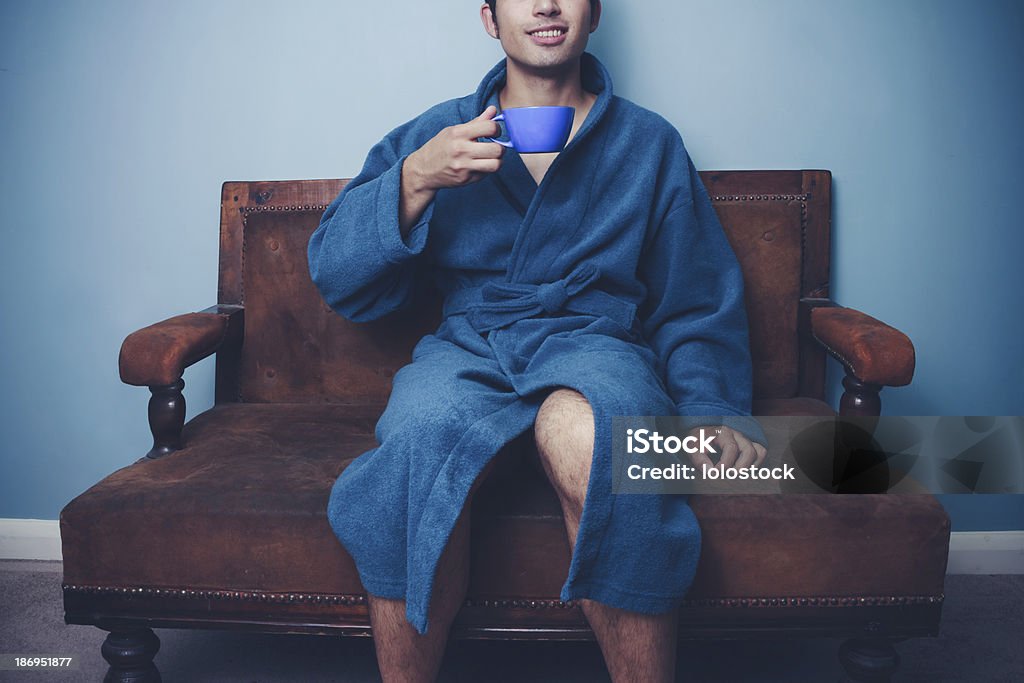 Giovane uomo in accappatoio bere caffè sul divano - Foto stock royalty-free di Uomini