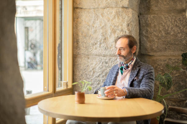 istock Senior man with beard looking out the window calmly sitting at a table in a cafe 1869522278