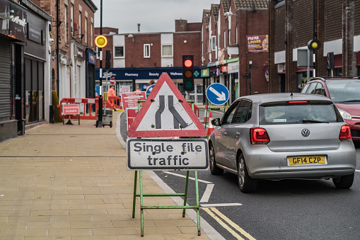 Nantwich, Cheshire, England, September 17th 2023. Silver car waiting in road work with a single file traffic sign, information editorial illustration.