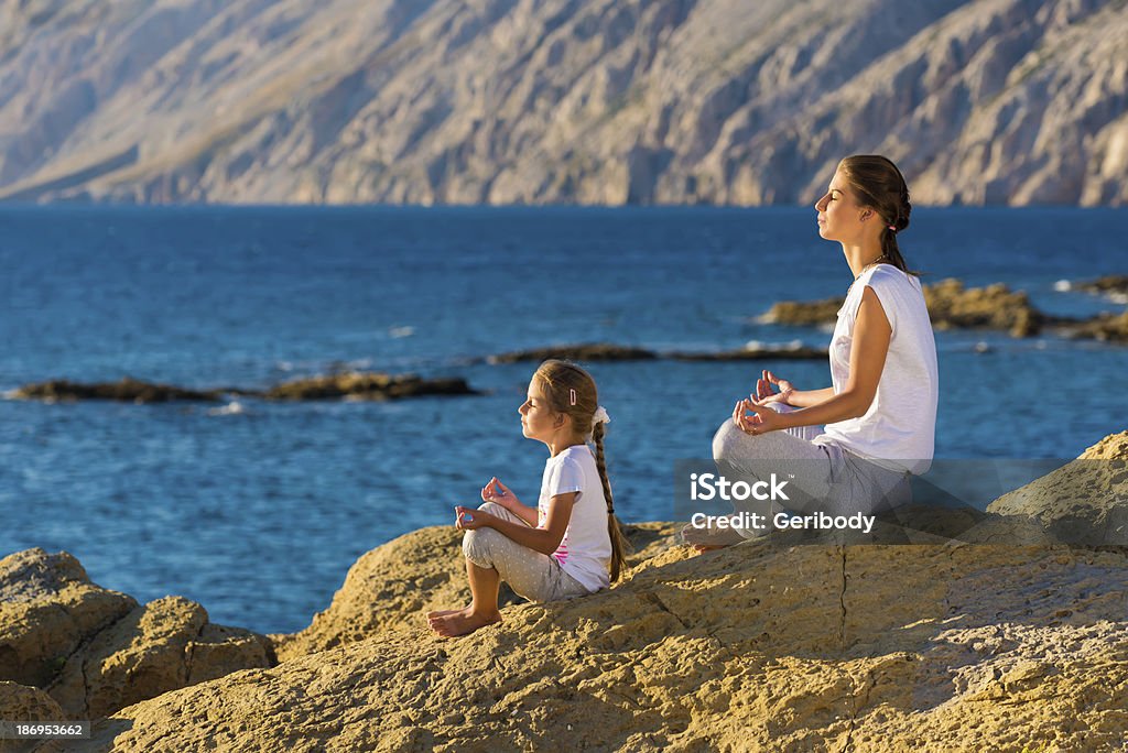 Mother and daughter doing yoga exercise on the beach Adult Stock Photo