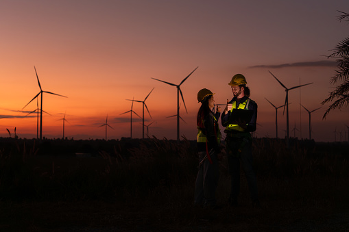 Engineers working on wind turbines farm at sunset, Wind turbines are alternative energy source.