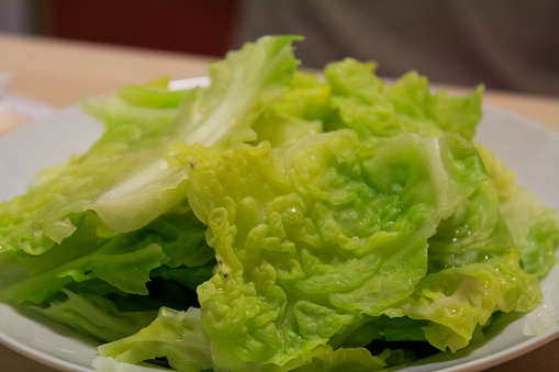 Horizontal high angle closeup photo of Cos lettuce leaves, chopped red capsicum and onion, shredded carrot and cabbage, herbs, cucumber slices and mung bean sprouts with a French vinaigrette in a grey ceramic serving dish on a wooden table in a Restaurantk