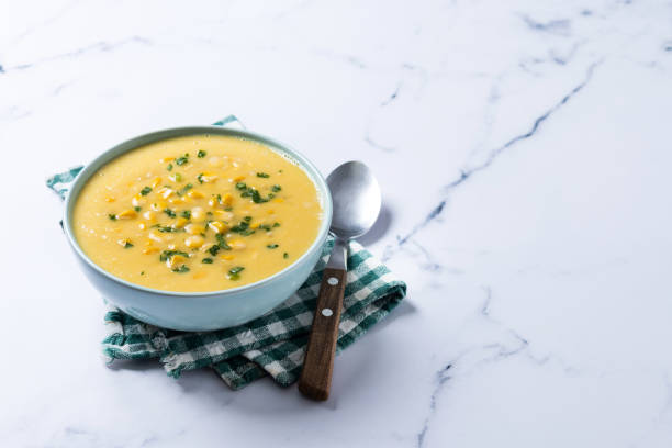 Corn soup in green bowl on white marble