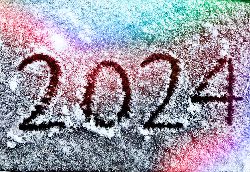 New Year 2024 handwriting on fresh snow with reflected Christmas lights representing colors of love and friendship, peace and unity, diversity, and happiness concepts