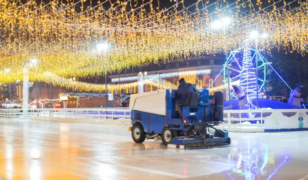 The ice rink in center of city park. Ice polishing with service machine at evening with garland