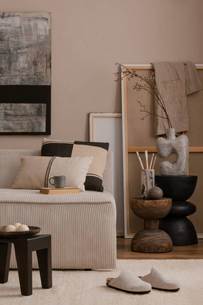 istock Stylish composition of warm living room interior with mock up poster frame, modular sofa, pillows, beige carpet, wooden stool, gray slippers, wooden stand and personal accessories. Home decor. Template. 1869598576