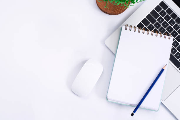 istock White desk with Laptop, blank notepad, flower and pen. Flat lay top view copy space. 1869598728