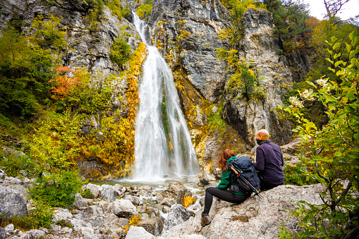 Two people sitting on a rock next to a natural waterfall. Shot in northern Albania near Theth.
