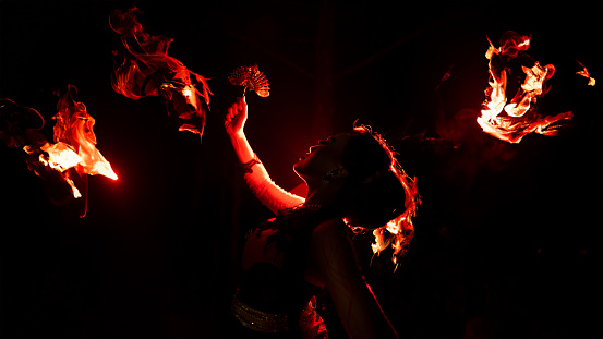 The silhouette of a female dancer holding jewelry in the dark of night is lit by the light of a burning fire and looks dramatic