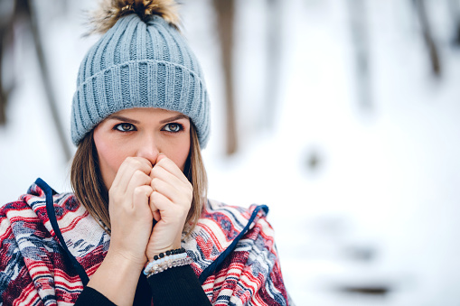 Beautiful young woman worming up her hands in a snowy park in winter.