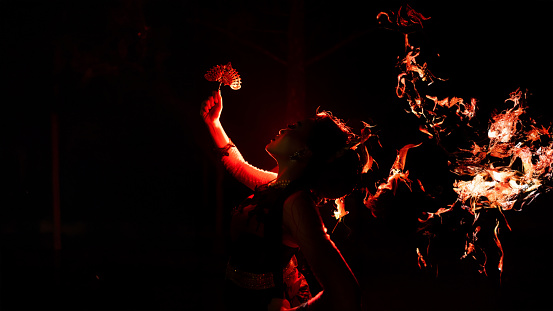 the silhouette of a female dancer holding sparkling jewelry and looking sharp in the dark with fire burning in the background at night