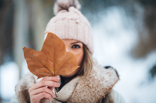 Portrait of a beautiful young woman holding a leaf in a snowy park in winter.