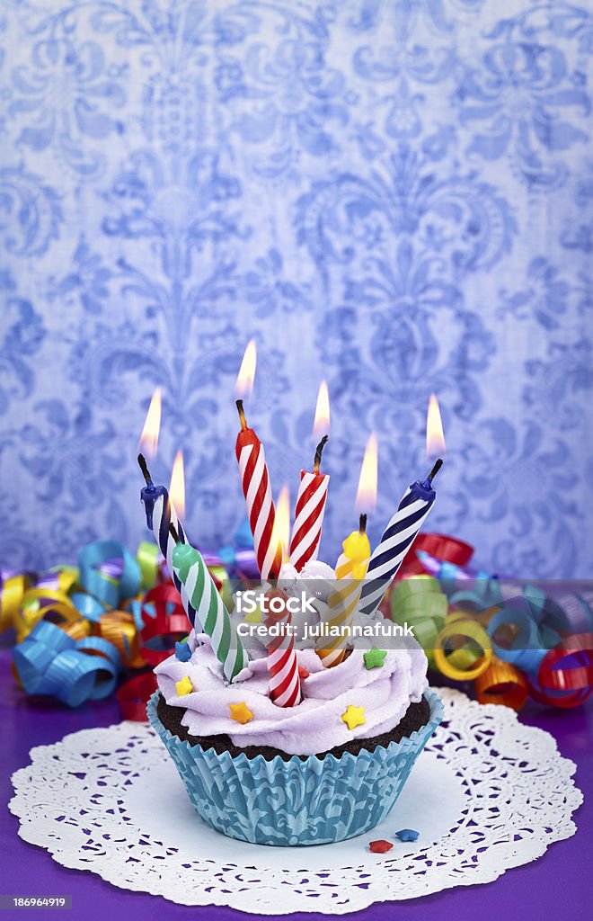 Birthday Cupcake Fun birthday cupcake loaded with candles and colourful sprinkles on a purple background with ribbons. Great for Birthday Parties. Baked Stock Photo