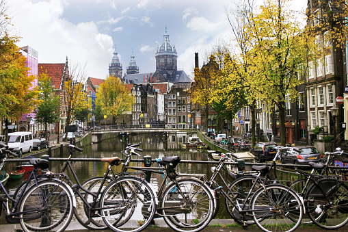 Bicycles leaning on the railing of a bridge over a canal in Amsterdam in autumn. In the background, the dome of Saint Nicholas