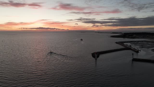 Small boat leaving Port Haliguen marina during sunset in Quiberon western Atlantic coast of France, Aerial rising pull out shot