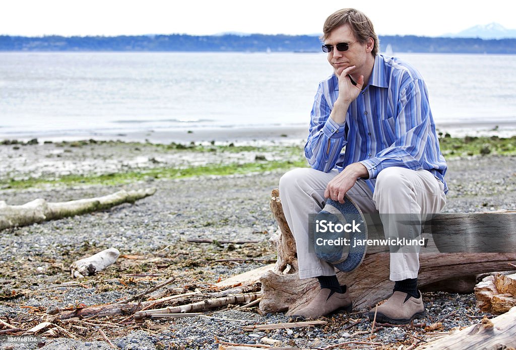 Depressed man sitting on driftwood along beach Depressed, sad Caucasian  man in forties sitting on driftwood on beach, chin in hand 40-49 Years Stock Photo