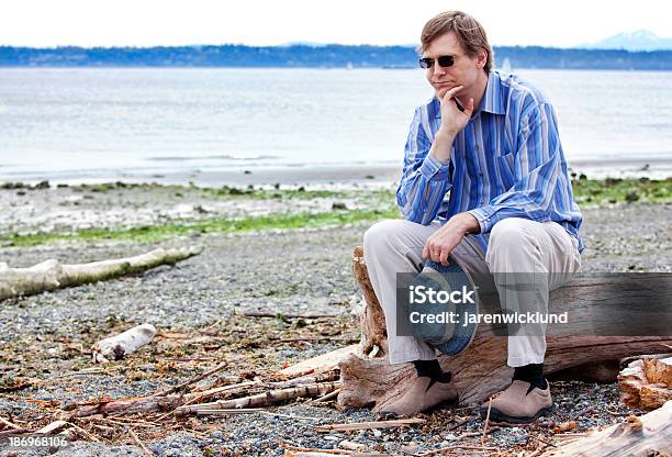 Depressed Man Sitting On Driftwood Along Beach Stock Photo - Download Image Now - 40-49 Years, Adult, Adults Only
