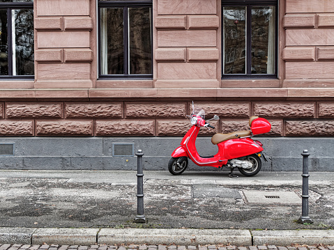 Red scooter on the sidewalk in front of a sandstone house.