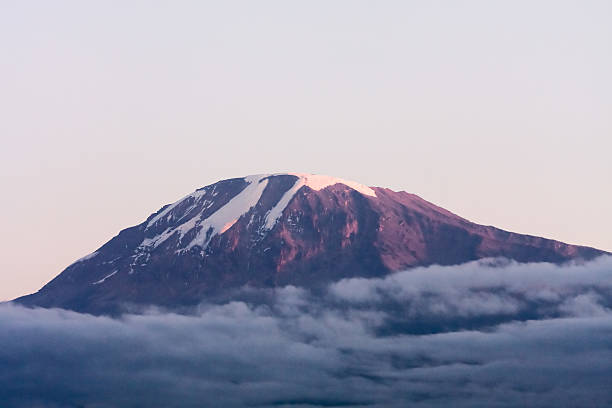 View on snow-covered Mount Kilimanjaro (extinct volcano) peak with cloud at sunrise light against sky background. Great Rift Valley, Tanzania, East Africa.
