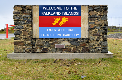 East Falkland, Falkland Islands: welcome to the Falkland Islands sign at Mount Pleasant Airport, stone wall with the British Joint Forces flag, horizontal tricolour of dark blue (Royal Navy) over red (Army) over air force (light) blue (Royal Air Force) with the map of the islands.