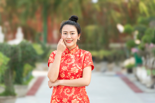 Asian woman wearing traditional cheongsam qipao dress with gesture of congratulation in Chinese Buddhist temple. Emotion smile new year concept