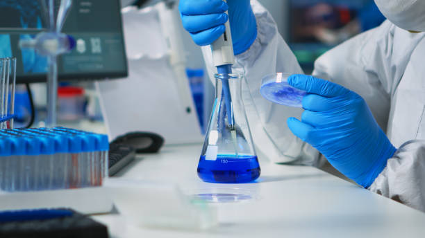 istock Doctor in ppe suit using pipette with microtiter plate and petri dish 1869717409