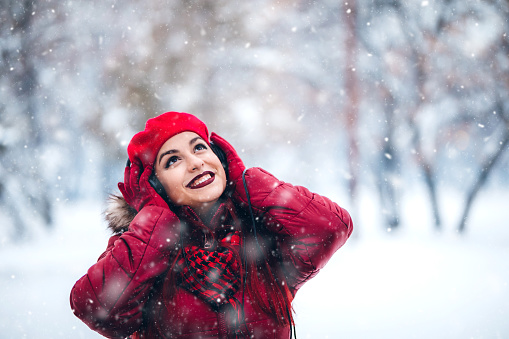 Beautiful young plus size woman listening to music via headphones in a snowy park in winter.