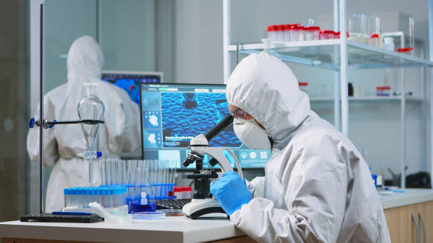 istock Chemist researcher in coverall looking at bacteria sample from glass 1869721680