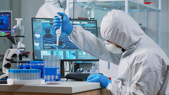 Scientist man pipetting liquid to test tube wearing protection suit in lab. Team of doctors examining virus evolution using high tech for scientific analysis of treatment development against covid19