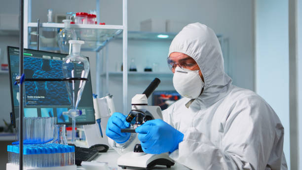 istock Scientist in ppe suit placing a slide on specimen stage 1869733035