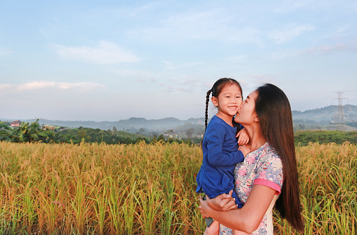 Happy Asian mother and daughters kissing in the meadow field at morning.