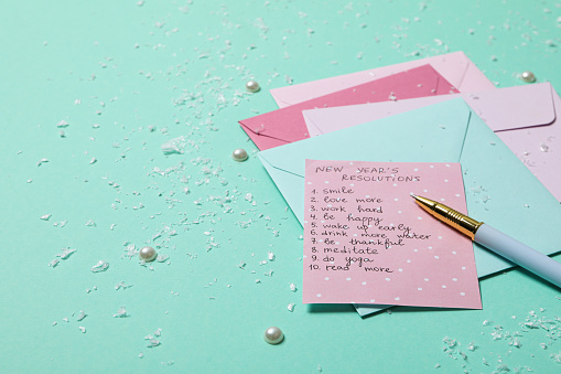 A thank you card on a pink envelope, with pink and white flowers on rustic wood background.\nShot from above.