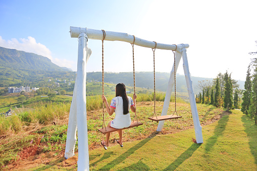 Back of young woman relaxing by swing on hillside at morning sunrise.